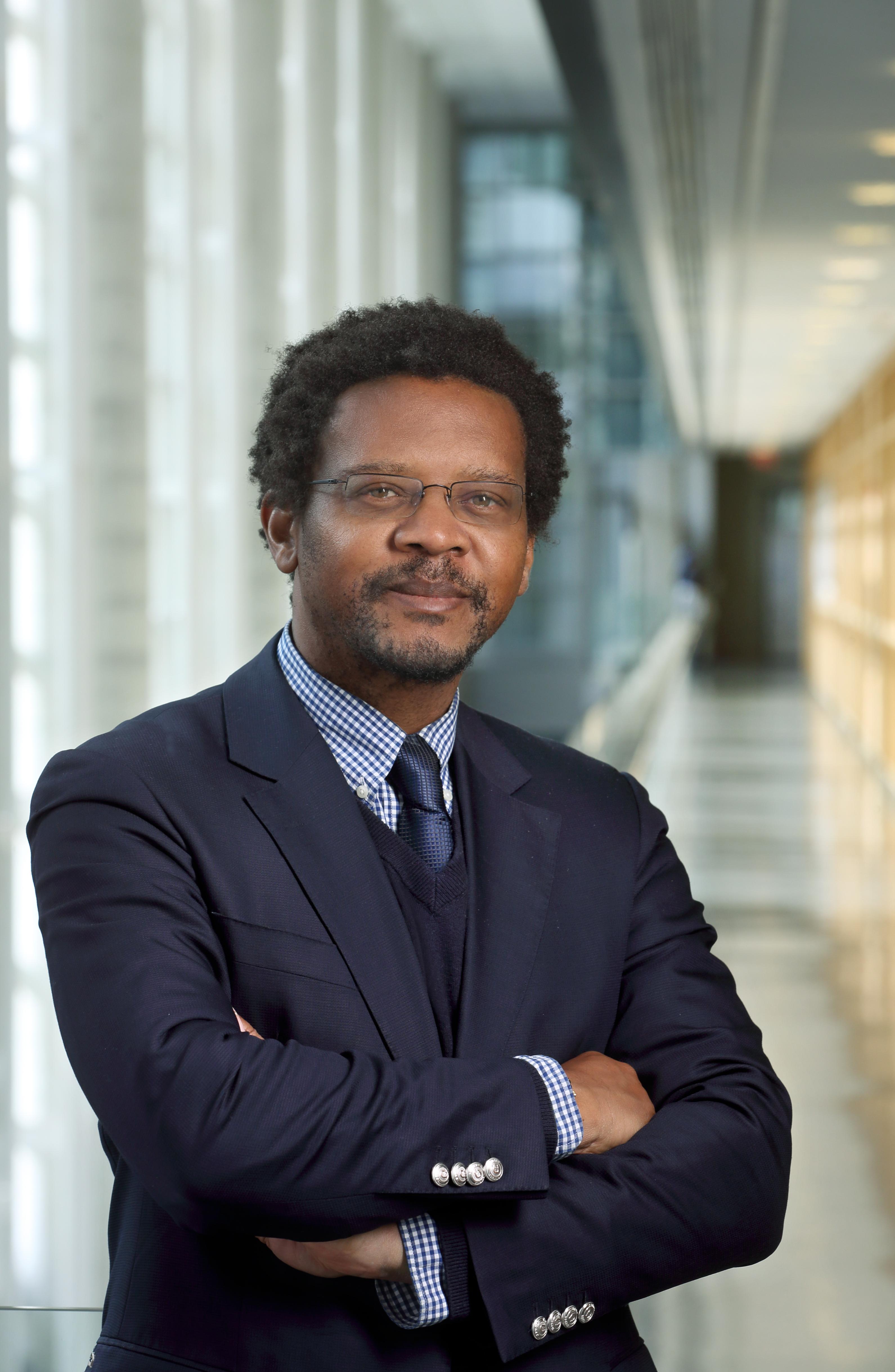 遗传医学部主任Ambroise Wonkam的肖像照. 他是一个非裔美国人，站在研究大楼的走廊上