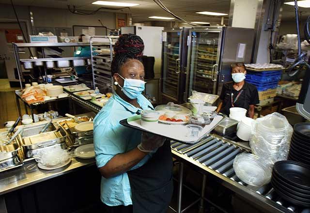 Food service employee wearing a mask with a tray.